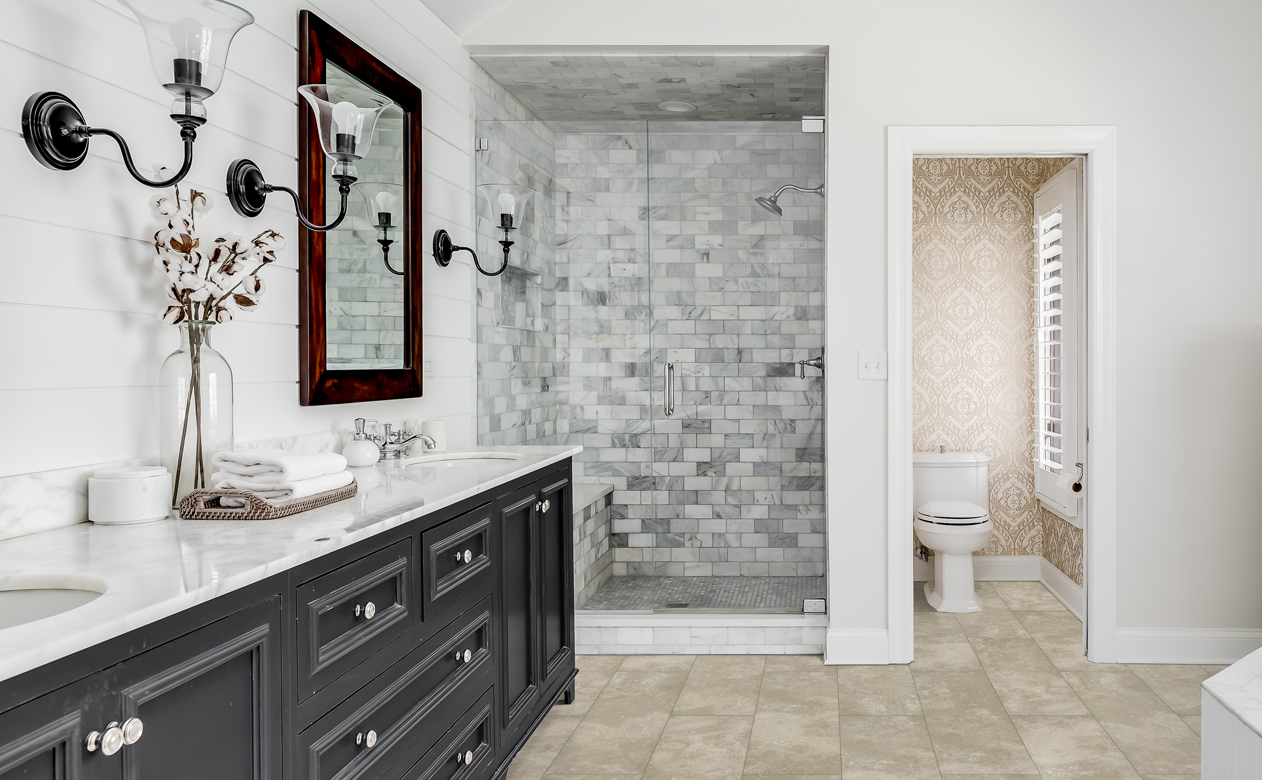 marble tile shower surround in bathroom with neutral waterproof flooring and dark vanity with white stone countertop and white wall shiplap